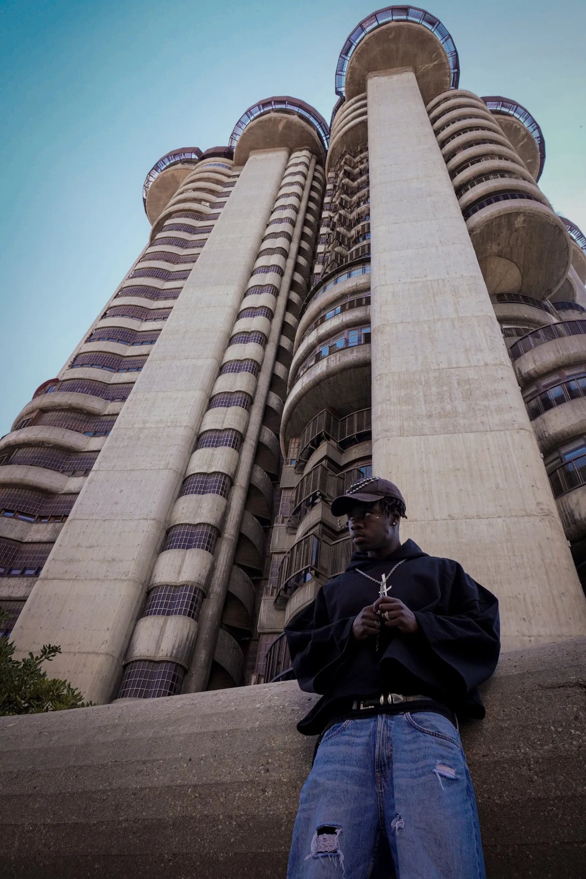 Modelo con sudadera negra y vaqueros anchos Skull Hearts Drop 02, foto contrapicada frente a edificio brutalista.